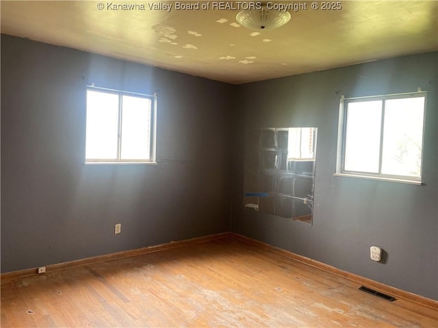 spare room featuring wood finished floors, visible vents, and a healthy amount of sunlight