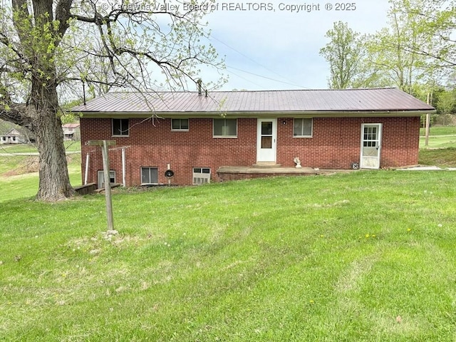 rear view of property featuring brick siding, a yard, and metal roof