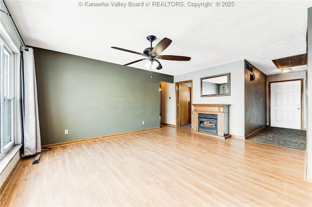 unfurnished living room with visible vents, a ceiling fan, light wood-type flooring, baseboards, and a glass covered fireplace