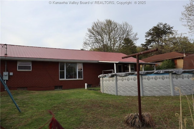 back of house with a lawn, a covered pool, brick siding, and metal roof