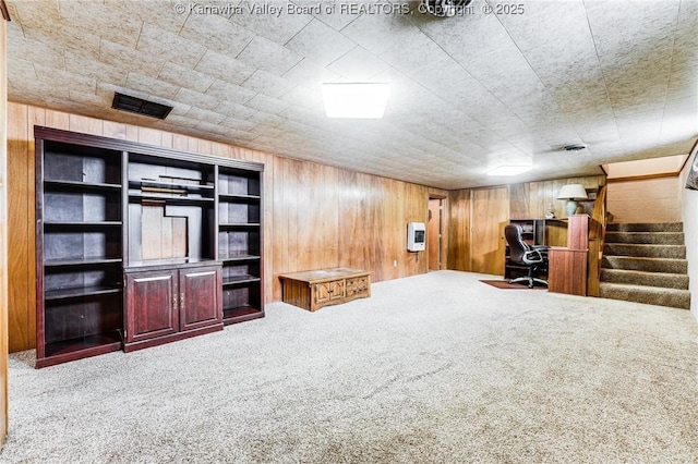interior space with visible vents, heating unit, stairway, wooden walls, and carpet floors