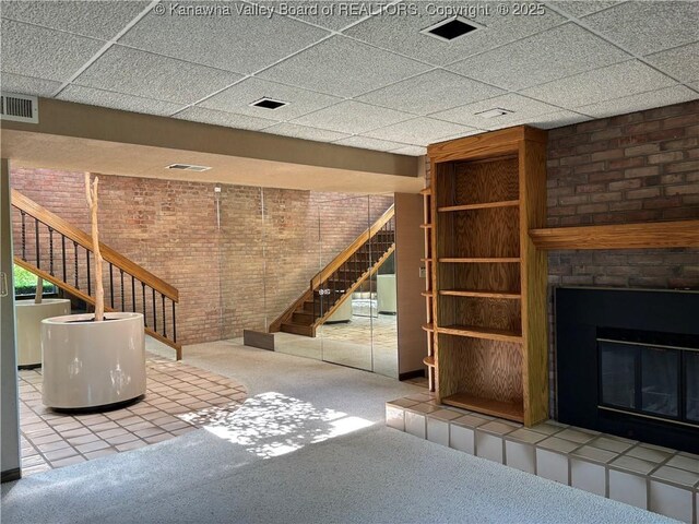 207 Mckinley Ave, Charleston, WV 25314 - unfurnished living room featuring brick wall, visible vents, a tiled fireplace, carpet floors, and stairs