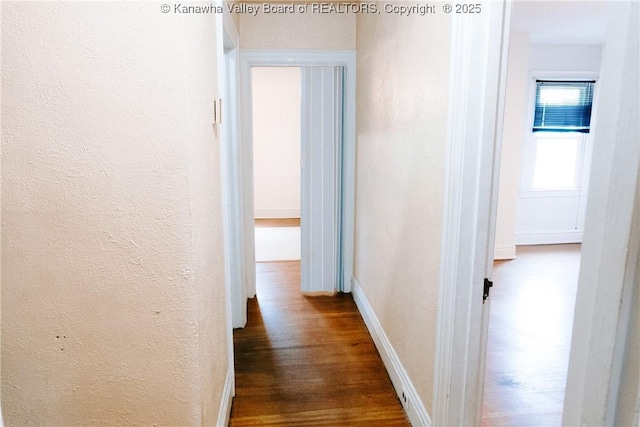 corridor featuring a textured wall, dark wood-style floors, and baseboards