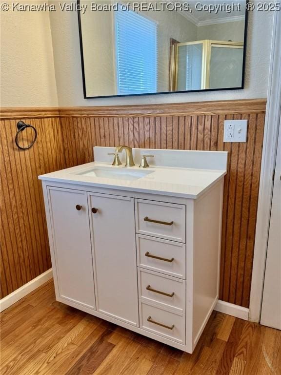 bathroom with wood finished floors, wooden walls, ornamental molding, and vanity