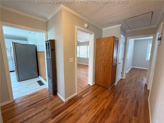 hallway with attic access, a heating unit, visible vents, a textured ceiling, and wood finished floors