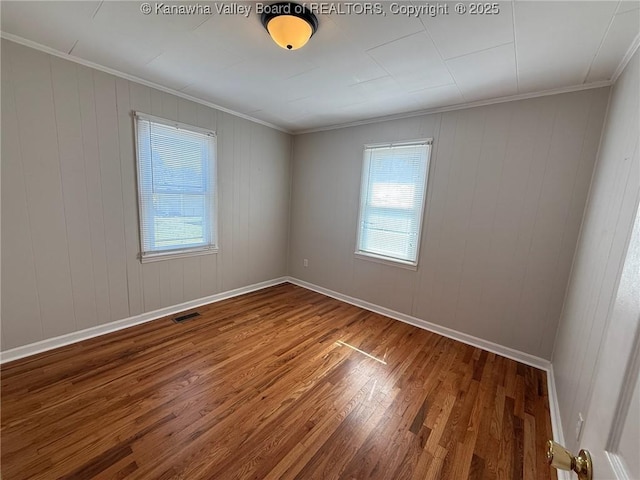 spare room with baseboards, visible vents, wood finished floors, and ornamental molding