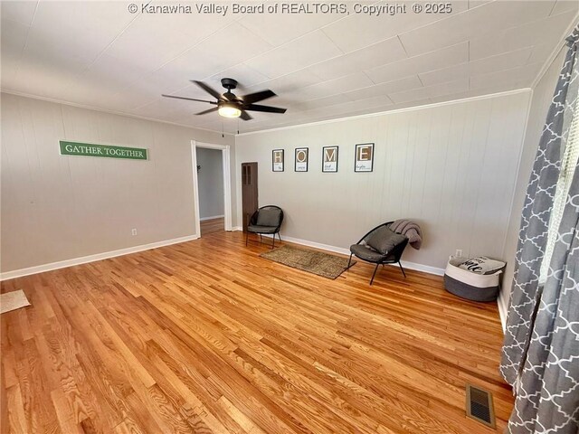 living area featuring crown molding, wood walls, visible vents, light wood-style floors, and a ceiling fan