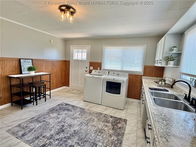 laundry room with a sink, washing machine and clothes dryer, marble finish floor, wood walls, and wainscoting