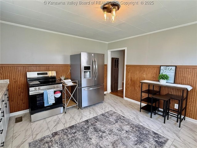 kitchen featuring stainless steel appliances, a wainscoted wall, marble finish floor, wood walls, and ornamental molding