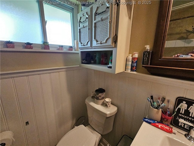 bathroom with a decorative wall, toilet, and wainscoting