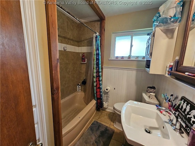 bathroom with tile patterned floors, wainscoting, shower / bath combination with curtain, toilet, and a sink