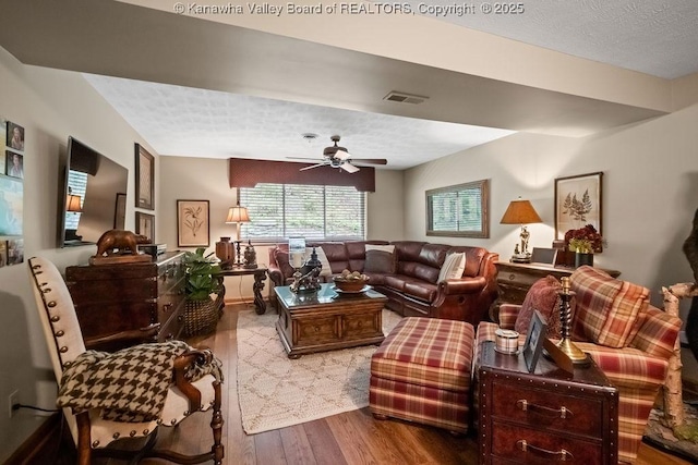 living area with a textured ceiling, ceiling fan, wood finished floors, and visible vents