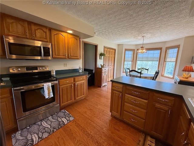 kitchen with light wood-type flooring, stainless steel appliances, dark countertops, and brown cabinets