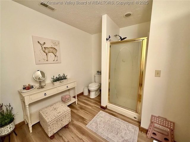 full bathroom with wood finished floors, a shower stall, toilet, visible vents, and a textured ceiling