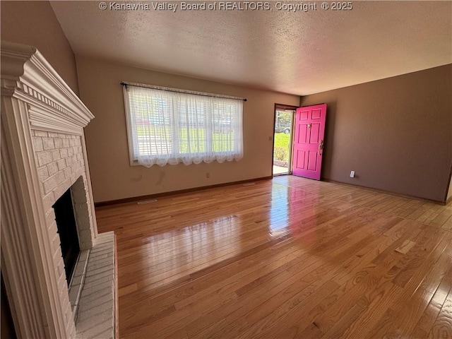 168 Jane Dr, Culloden, WV 25510 - unfurnished living room featuring a brick fireplace, a textured ceiling, hardwood / wood-style floors, and baseboards
