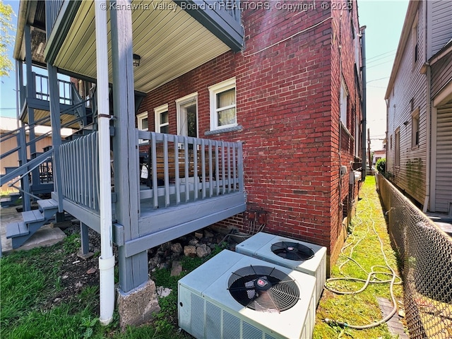 view of property exterior with brick siding, central air condition unit, stairway, and fence