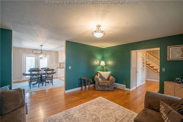 living area with stairs, light wood-style floors, and baseboards