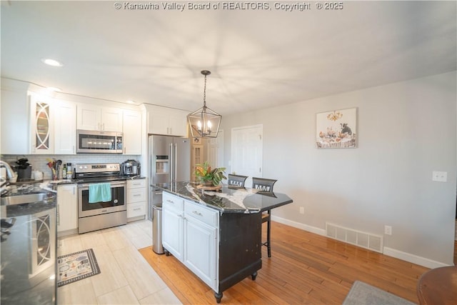 kitchen featuring appliances with stainless steel finishes, a sink, white cabinetry, a kitchen breakfast bar, and baseboards