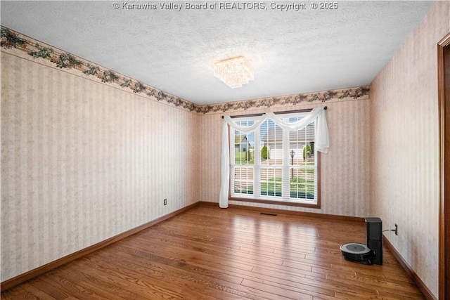 spare room featuring baseboards, hardwood / wood-style floors, and wallpapered walls