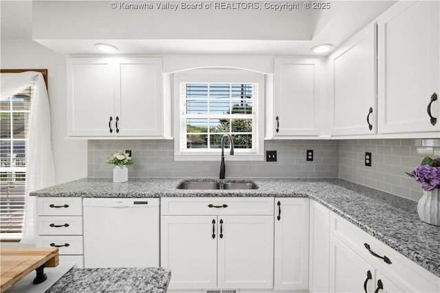 kitchen with a sink, white dishwasher, light stone countertops, and white cabinetry