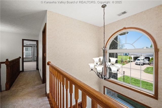 hallway with visible vents, carpet floors, a chandelier, and an upstairs landing
