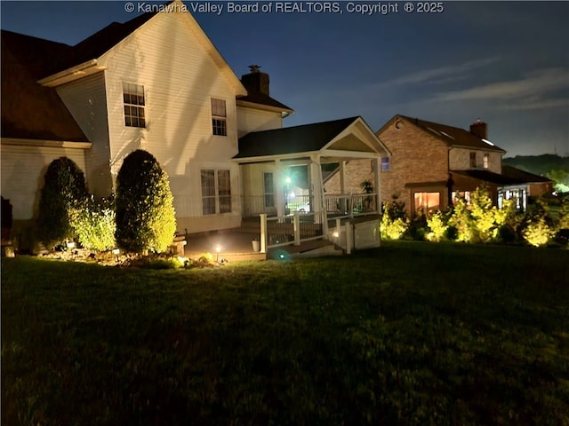 back of house at night featuring a lawn, a patio, and a chimney