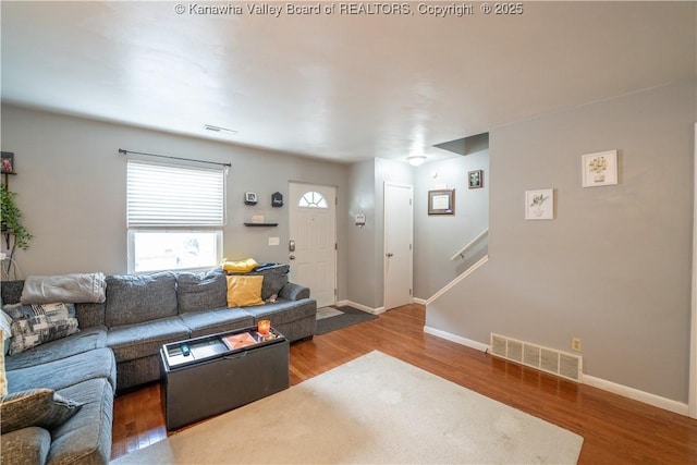 living room featuring visible vents, stairs, baseboards, and wood finished floors