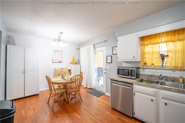 kitchen featuring decorative backsplash, a sink, an inviting chandelier, stainless steel appliances, and white cabinetry
