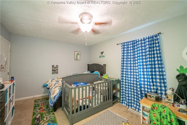 bedroom with a ceiling fan, a textured ceiling, a nursery area, baseboards, and carpet flooring