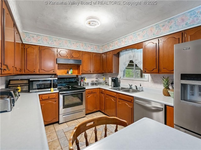 kitchen with a sink, appliances with stainless steel finishes, under cabinet range hood, and light countertops