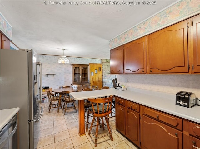 kitchen featuring brown cabinetry, light countertops, stainless steel appliances, wallpapered walls, and light tile patterned flooring