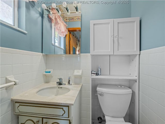 bathroom with toilet, tile walls, plenty of natural light, and vanity