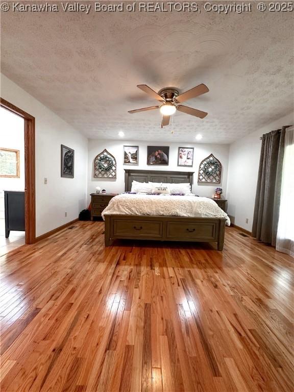 bedroom featuring baseboards, a ceiling fan, a textured ceiling, and light wood-style flooring