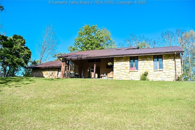 back of property featuring a lawn, metal roof, and stone siding