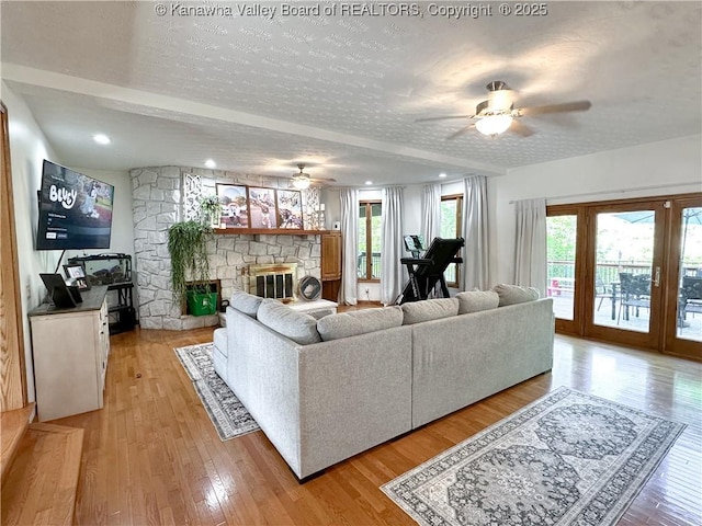 living area featuring a textured ceiling, ceiling fan, light wood-type flooring, and a stone fireplace