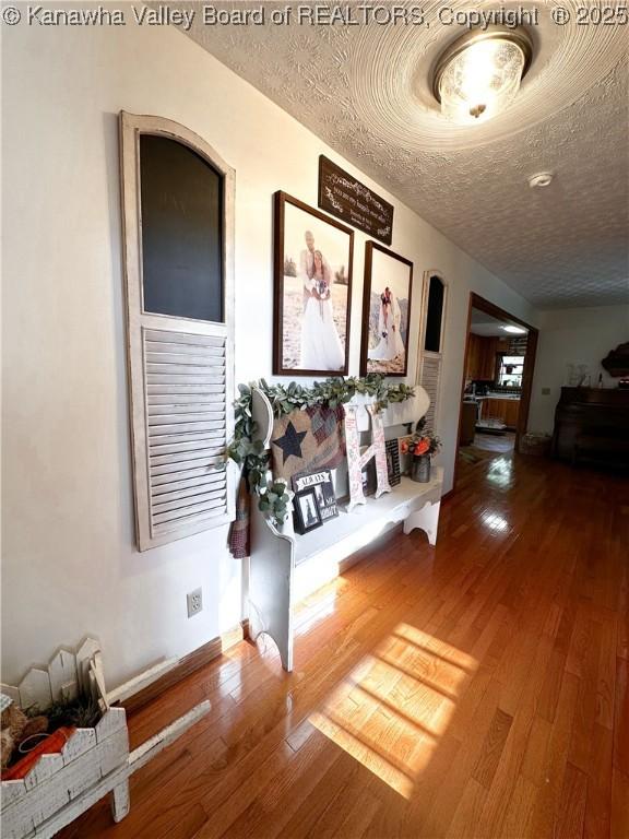 hallway featuring a textured ceiling, baseboards, and wood finished floors