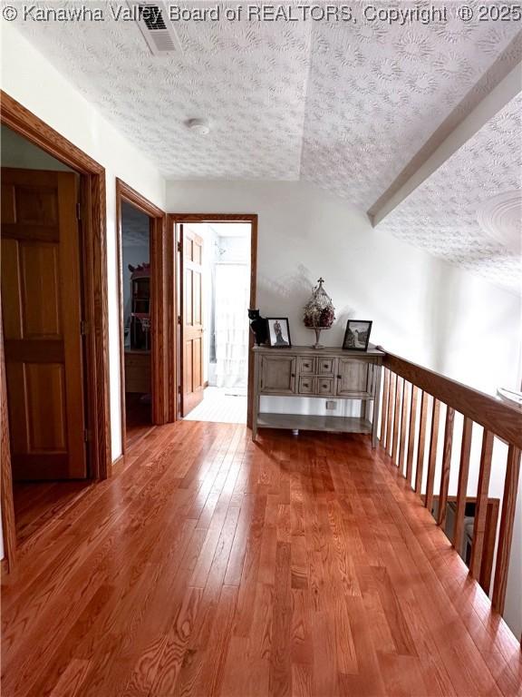 corridor featuring a textured ceiling, wood finished floors, and visible vents
