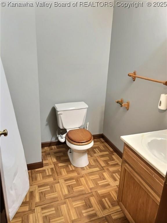 half bath featuring baseboards, vanity, and toilet