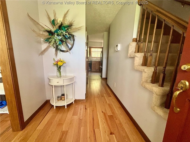 hallway with light wood-type flooring, a textured ceiling, baseboards, and stairway