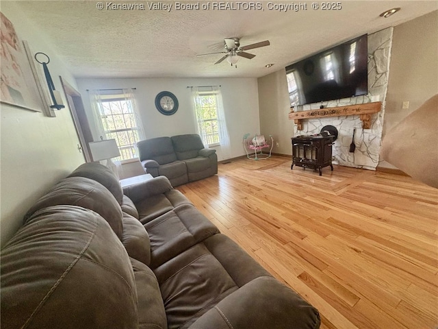 living area with a textured ceiling, ceiling fan, a stone fireplace, and hardwood / wood-style flooring
