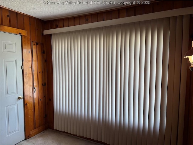 unfurnished room with radiator heating unit, wood walls, a textured ceiling, and light colored carpet