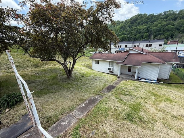 rear view of property with a lawn, roof with shingles, a forest view, and a porch