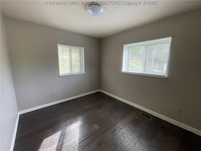 empty room with a healthy amount of sunlight, baseboards, dark wood-style flooring, and visible vents