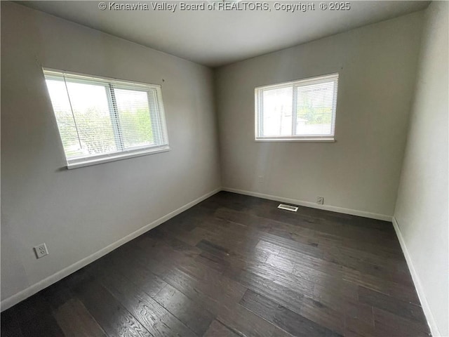 spare room with baseboards, visible vents, a wealth of natural light, and hardwood / wood-style floors
