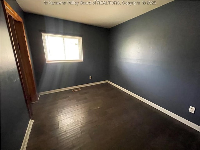 spare room with visible vents, baseboards, and dark wood-type flooring