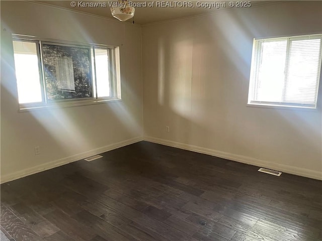 spare room with baseboards, dark wood finished floors, ornamental molding, and visible vents