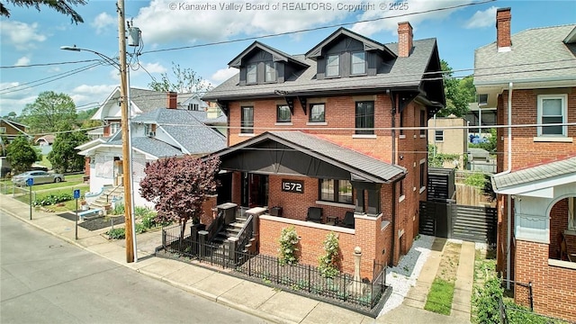 view of front of property with a porch, brick siding, a fenced front yard, and roof with shingles
