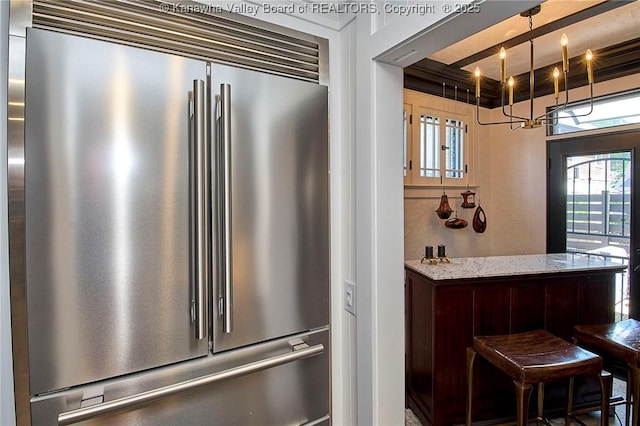 kitchen with an inviting chandelier, light stone countertops, and high end fridge