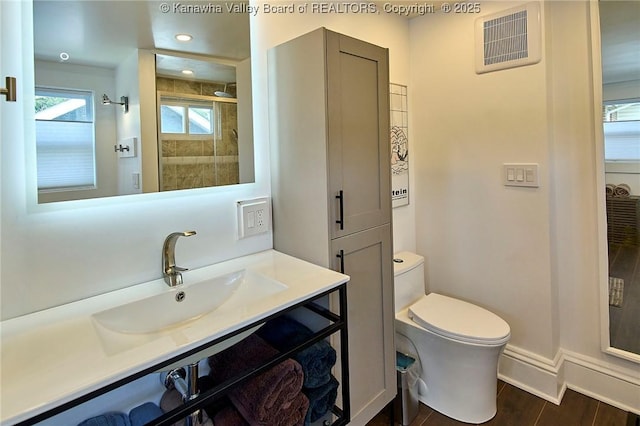 bathroom with visible vents, vanity, baseboards, toilet, and tiled shower