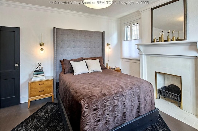 bedroom with ornamental molding, wood finished floors, and a tile fireplace